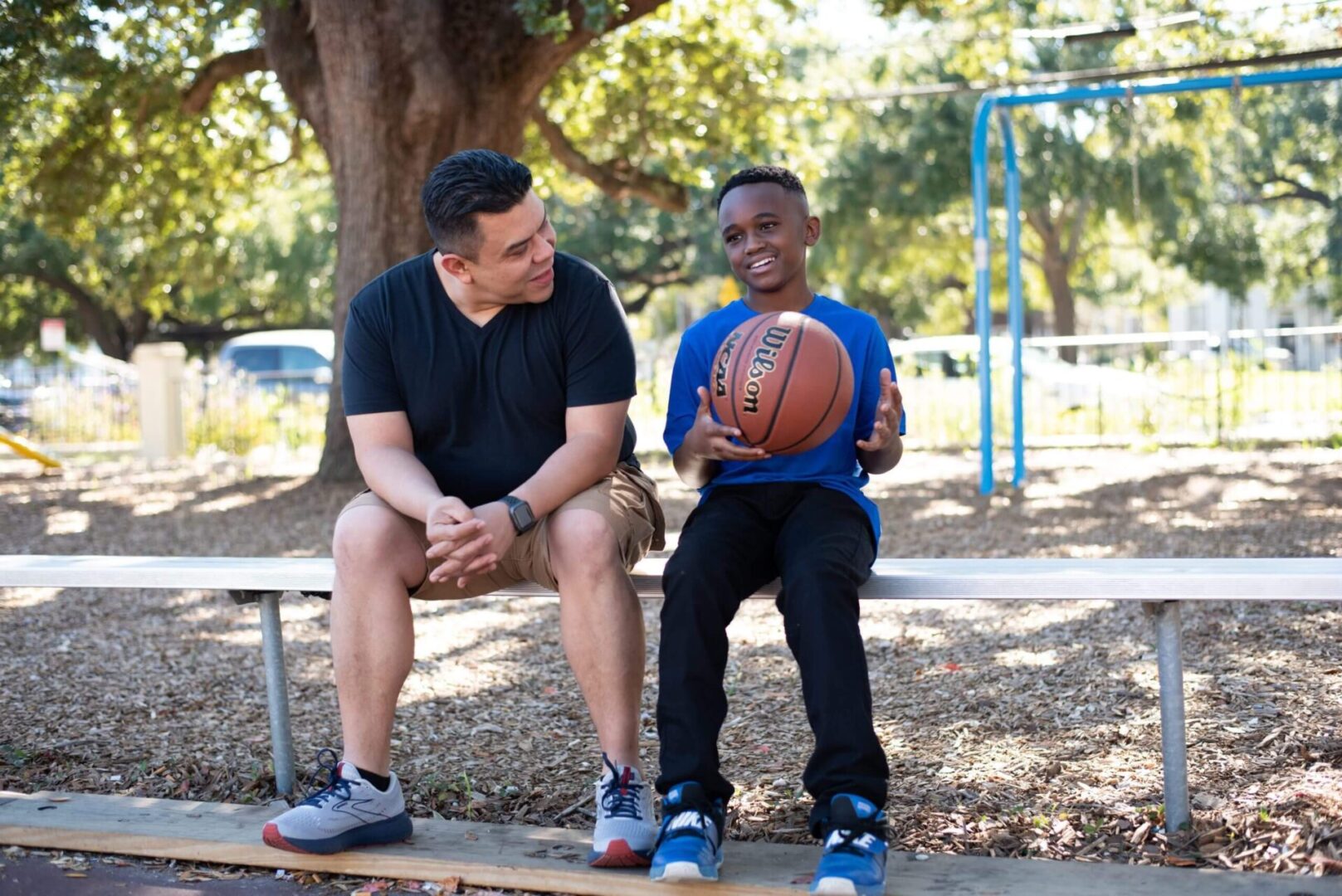 A man and boy sitting on a bench with a basketball.