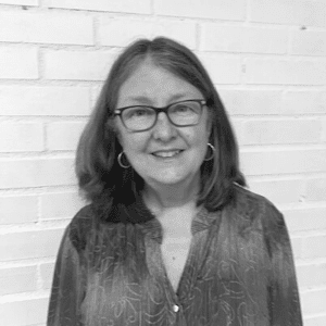 A black and white photo of a woman in front of a brick wall.