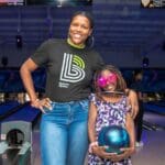 A woman and girl posing for the camera at an indoor bowling alley.